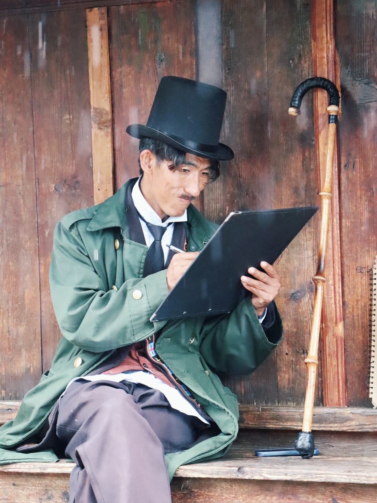 一个老人戴着绿色帽子坐在木质台阶上 手里拿着拐杖和雨伞。