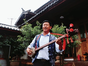 一位男子站在一所房子前面 手里拿着一把传统的中国吉他。