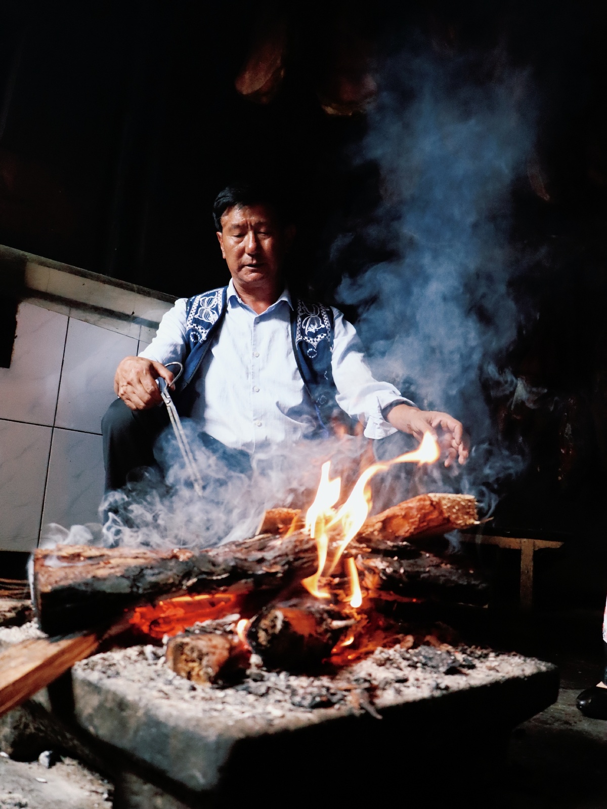 一个在开放火焰上使用大型烧烤架烹饪食物的男子。