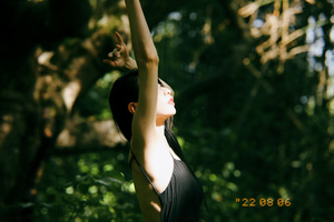 一个年轻女子站在树林里 双臂高举 空中有一个飞盘