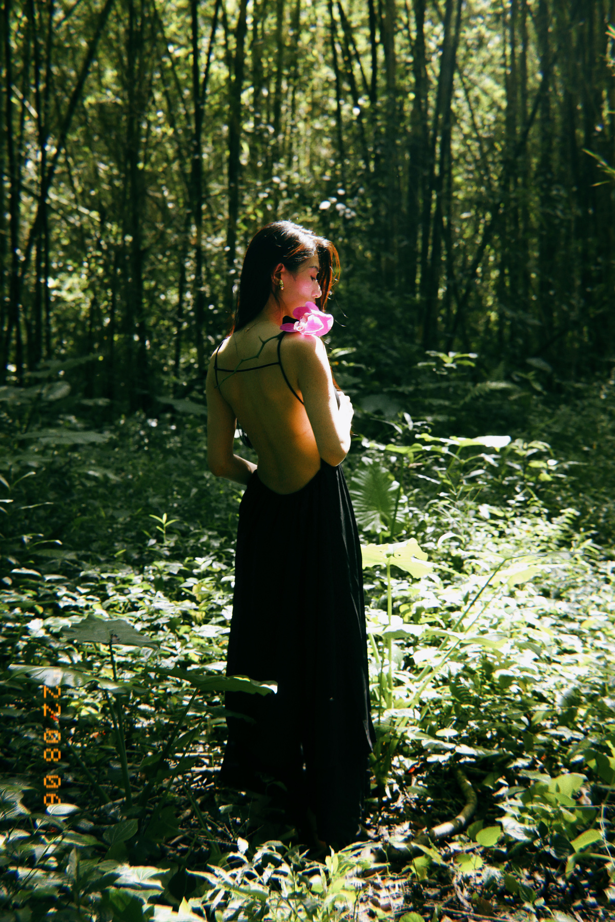 一位身穿黑色连衣裙、手持鲜花的年轻女子站在树林中