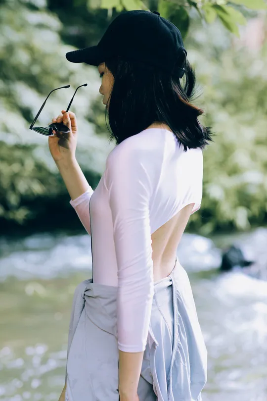 一位穿着白色衬衫、粉色裙子和帽子的女人站在河边。