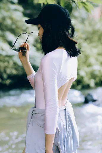 一位穿着白色衬衫、粉色裙子和帽子的女人站在河边。