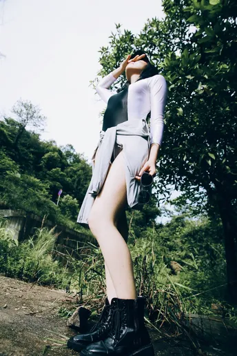 一位穿着黑色靴子的女人站在一棵树旁边