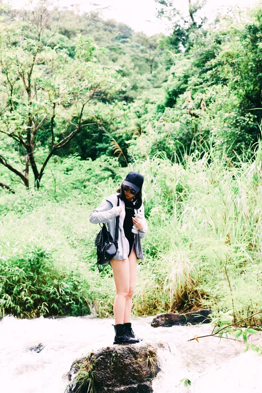 一位女性站在森林中的小溪或河流上的岩石上 手里拿着相机。