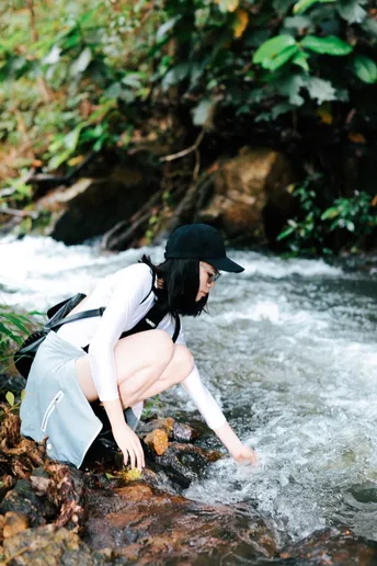 一个戴黑色帽子的年轻女子在一个河或小溪边的岩石上蹲着