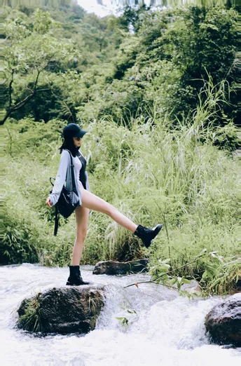 一位年轻女子背着背包站在一条溪流中的岩石上 位于森林中。