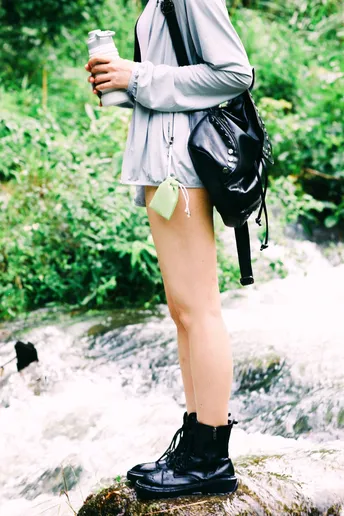 一个年轻女子穿着雨伞 端着一杯咖啡站在森林中的一条小溪边的岩石上。