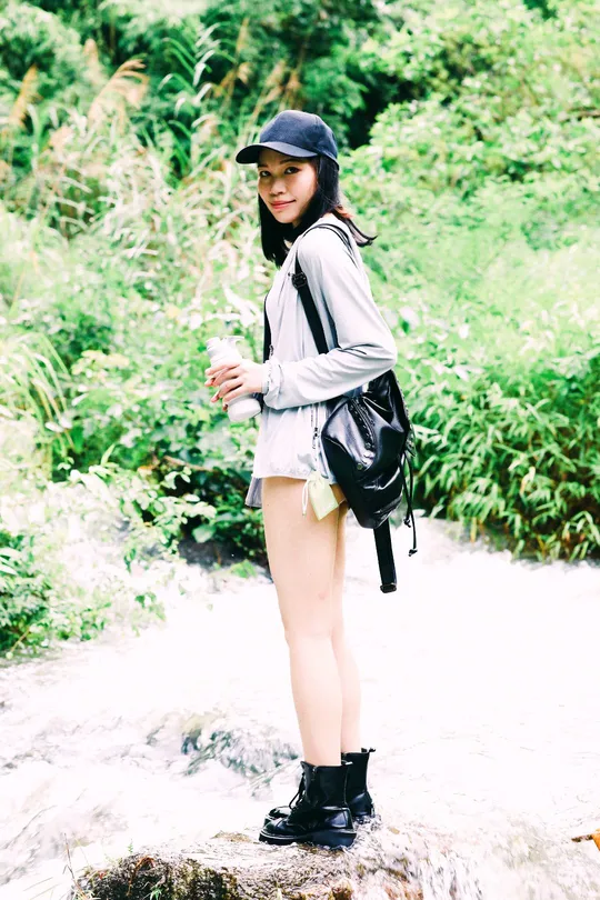 一个戴黑色帽子背书包的年轻女子站在森林中的岩石上