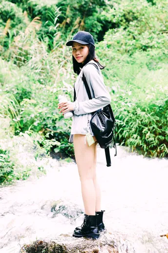 一个戴黑色帽子背书包的年轻女子站在森林中的岩石上