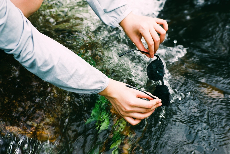 一个人站在河或小溪中的岩石上 手里拿着一只鞋。