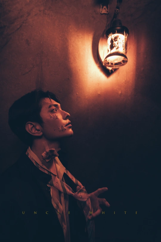 一个穿着西装打领带的年青男子站在一个光线昏暗的房间里 墙上有一个灯泡。