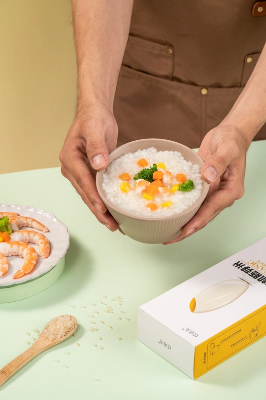 一个人在桌子前拿着一个小碗米饭和食物盒子