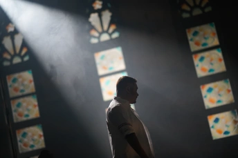 一个带有彩色玻璃窗的黑暗房间 一束光线透过窗户照射进来 一个人站在窗户前。