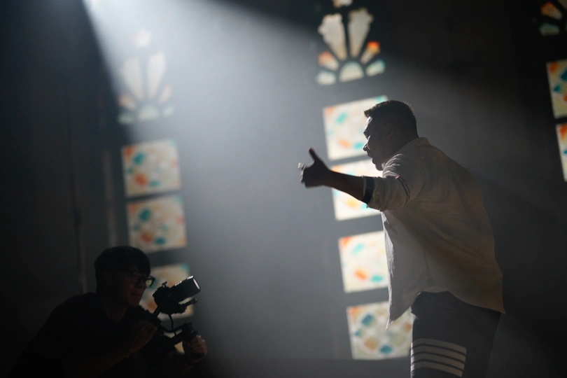 一个站在由彩色玻璃窗照射的房间里 舞台上冒出烟雾的男人带着相机。