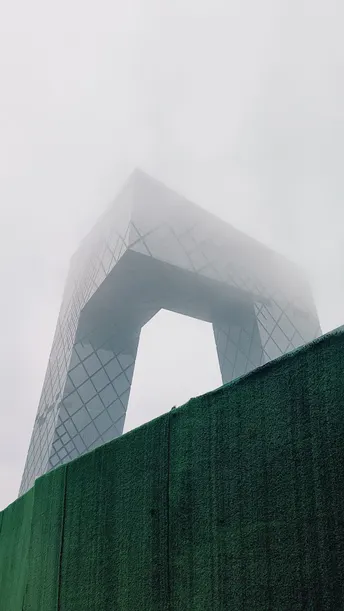 雾气缭绕的绿色围墙后面的高楼顶部