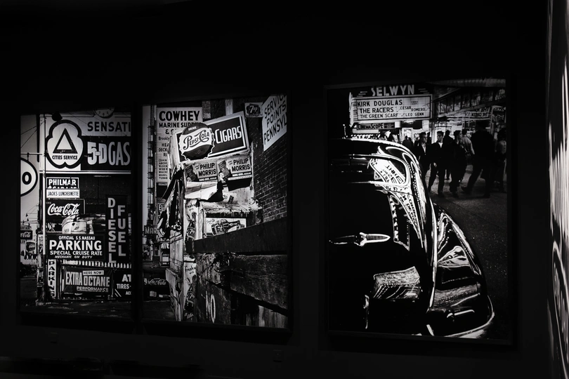 一张黑白照片 墙上贴着海报、标志和一辆停在街道上的汽车。