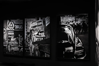 一张黑白照片 墙上贴着海报、标志和一辆停在街道上的汽车。