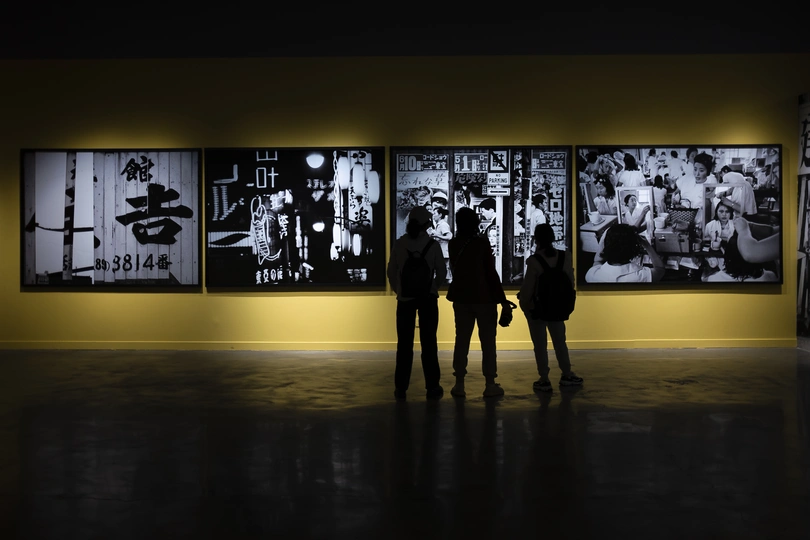 一张黑白照片 人们站在一个黄色的房间里 注视着墙上的艺术作品。