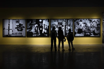 一张黑白照片 人们站在一个黄色的房间里 注视着墙上的艺术作品。