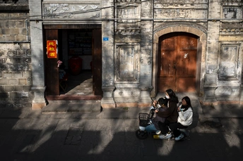 一个男子骑着滑板车沿着一座老建筑旁的街道驶过 一名女子坐在车的前面。