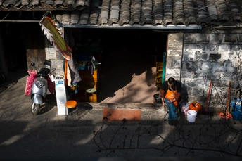 一个人坐在一个小建筑物外面 摩托车和滑板车在前面 外面有站着的人。