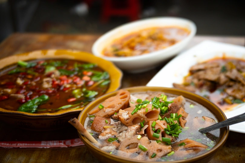 一个木制桌子 上面放着装满汤和肉的盘子和碗。