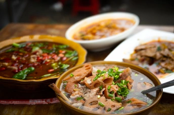 一个木制桌子 上面放着装满汤和肉的盘子和碗。