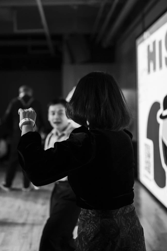 一张黑白照片 一个年轻女孩在和其他人一起玩电子游戏 周围站着其他人。