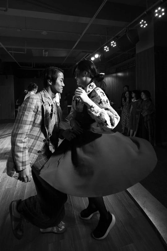 一张黑白照片 描绘了一对男女在舞台上跳舞 背景中还有其他人。