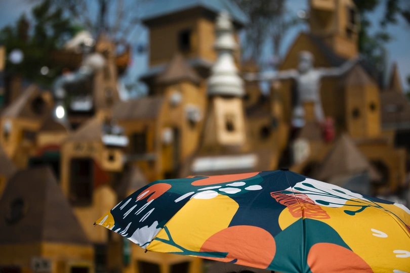 一个人手持彩色雨伞 背景中有微缩建筑。