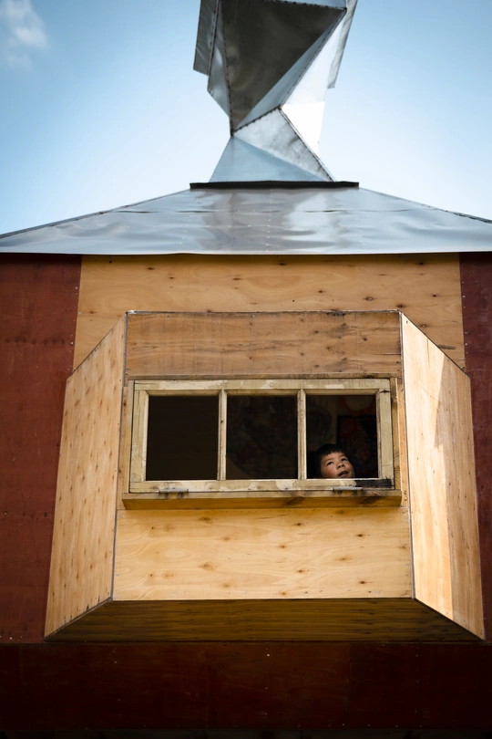 一个小男孩和一个女孩正在观察一个小建筑物的窗户。