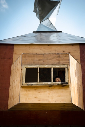 一个小男孩和一个女孩正在观察一个小建筑物的窗户。