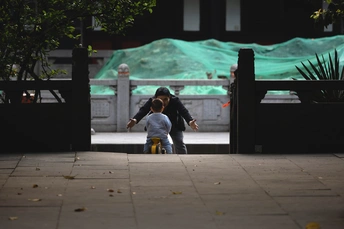 一个年轻男子在晚上骑自行车带着一个小男孩在人行道上行驶 同时街上有一个男子带着滑板手牵着他的手。