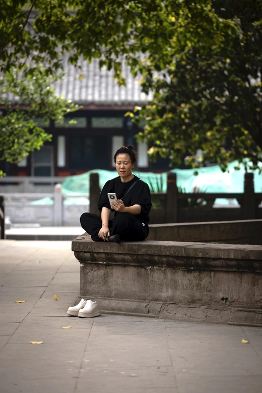 一个坐在人行道长椅上的男人 旁边有一个正在玩手机的女人。