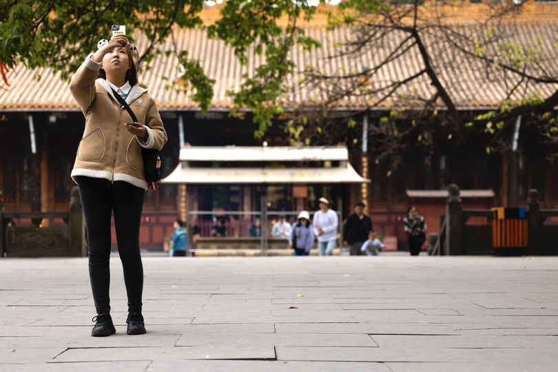 一位年轻女子站在街角大楼前 手中拿着手机。