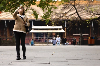 一位年轻女子站在街角大楼前 手中拿着手机。