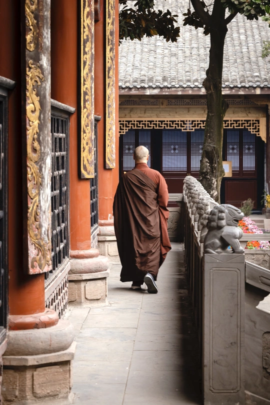 一个人穿着长袍走在一栋楼房旁边的人行道上