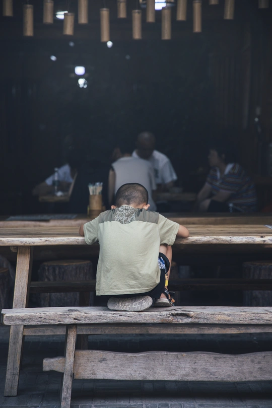 一个小男孩坐在木凳上 在一位坐在桌子前的男子面前。