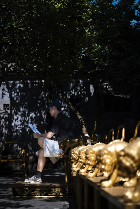 一个年轻男子坐在一个金色雕塑前面的一张长椅上。