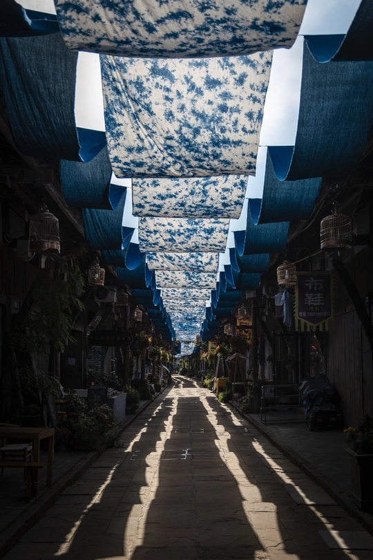 一条带有蓝色屋顶和伞的巷子 伞在天空下投下长长的阴影。