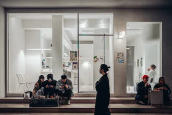 夜晚时分 一个人站在窗户前 周围有几个人坐着。