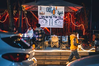 一个在舞台上演奏音乐的男子 周围有一些人在走 夜晚的亮着灯的街道。