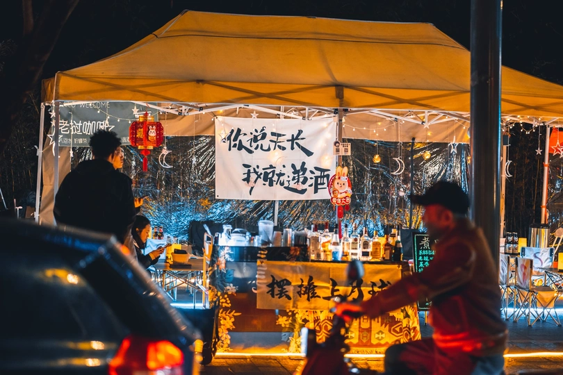 夜晚街道上有一顶帐篷 人们站在那里 一个人骑着自行车在伞下。