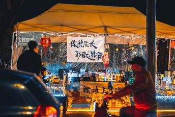 夜晚街道上有一顶帐篷 人们站在那里 一个人骑着自行车在伞下。