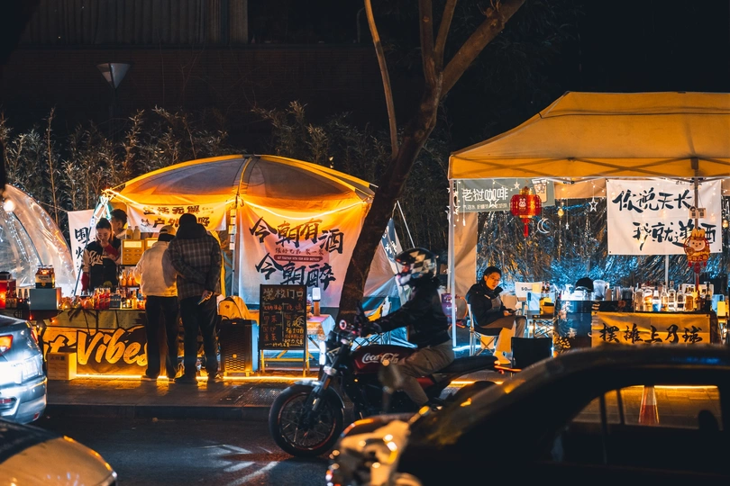 夜晚的街道上有帐篷、汽车和摩托车上的人们。