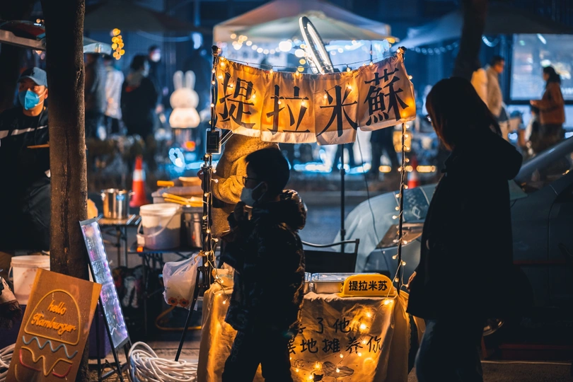 一位妇女在夜晚的市场下方的标志下站立