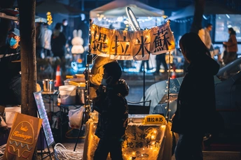 一位妇女在夜晚的市场下方的标志下站立