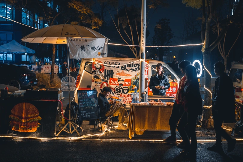 晚上街上的人们带着食物卡车和遮阳伞走动。