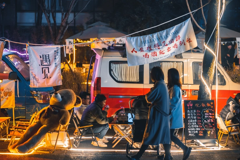 一些人坐在食品卡车旁边的一排椅子上。